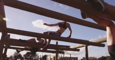 İki beyaz kadının alçak açılı görüntüsü ve bir acemi birliği eğitim seansı sırasında bir spor salonunda direkler arasından tırmanan beyaz bir genç adam.