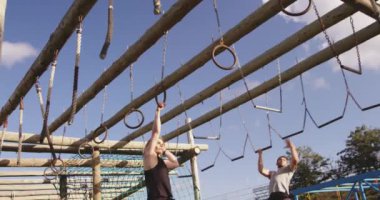 Genç beyaz bir kadın ve beyaz bir adamın, bir acemi birliği eğitim seansı sırasında halat ve halatlara asılı bir şekilde tırmanma iskelesinden geçerken ön görüntüsü.