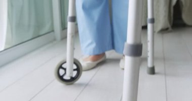 Genç bir karışık ırk kadın hemşire düşük bölümü olgun bir karışık Yarış adam bir yürüyüş çerçevesi kullanarak yürümek yardım
