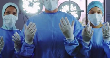 Hastanedeki ameliyathanede dikilirken el kol hareketi yapan cerrahların önü. Kameraya bakıyorlar.