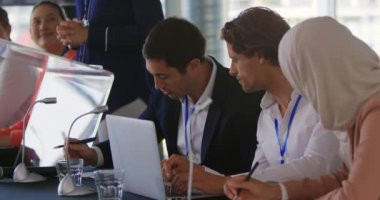 Kafkasyalı iki genç iş adamı ve kafatası ile tesettürlü bir iş kadınının yan görüntüsü kameraya arkasını dönmüş, oturuyor, notlar alıyor ve bir iş konferansında kendi aralarında konuşuyorlar.
