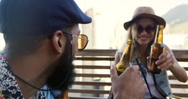 Yan manzara, mutlu, genç, melez bir erkeğin ve çatıdaki bir partide eğlenen ve bira içen Kafkas bir kadının yan görüntüsü.