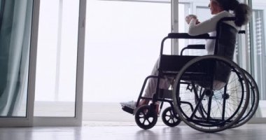 Tekerlekli sandalyede bir fincan kahve içen ve pencereden dışarı bakan olgun bir karışık Yarış kadının Yan görünümü