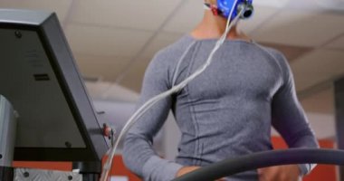 Bir koşu bandı üzerinde çalışan ve eğitim sırasında bir metabolik gaz analizörü kullanarak genç bir karışık ırk adam yakın, bir yüz maskesi giyen