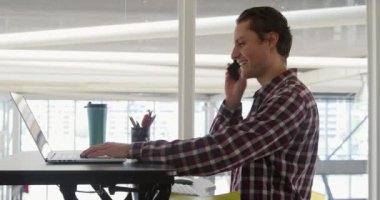 Modern bir ofiste çalışan, dizüstü bilgisayar, akıllı telefon kullanan ve kameraya gülümseyen mutlu beyaz erkek iş dünyasının portresi.
