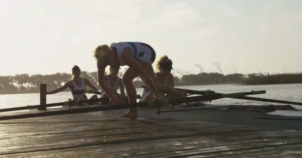 川の桟橋でレースシェルを着陸する4人の若い成人白人女性の漕ぎ手のチームの側面図 — ストック動画