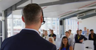 Kafkasyalı orta yaşlı bir iş adamının, mikrofon takıp sahnede durup bir iş konferansında seyircilere el kol hareketi yapmasını yakından izliyoruz. Oturan seyirci arka planda ona bakarken görülüyor.