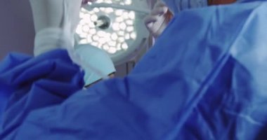 Ameliyathanede erkek doktorun cerrahi maske takmasına yardım etmek için yardımcı olan kadın doktorun yakın çekimi. Onlar operasyon için hazırlanıyor, video