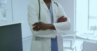 Afro-Amerikan erkek doktorun ön görünümü hastanede kolu çapraz ayakta. O gülümsüyor ve kamera, video bakıyor