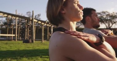 Kafkasyalı genç bir kadın ve beyaz bir adamın, acemi birliği eğitimi sırasında açık hava spor salonunda genç bir beyaz kadın eğitmenle mekik çekerken yan görüntüsü.