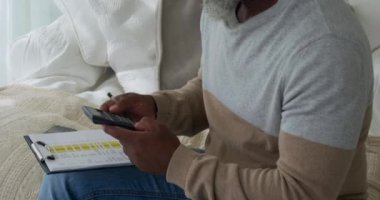 Bir hesap makinesi kullanarak ve evde bir pano ya yazma olgun bir karışık ırk adam yan görünümü yakın