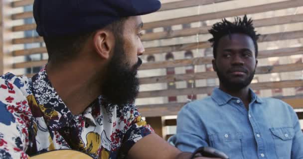 一位年轻的混血儿拿着吉他 与一位年轻的非洲裔美国男性朋友聊天 在屋顶上的一个派对上自得其乐 侧观近景 — 图库视频影像