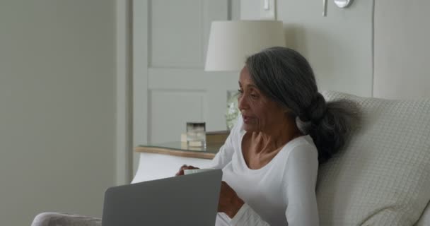 自宅で話すベッドに座ってラップトップコンピュータを持つ成熟した混合レースカップルの側面図 — ストック動画