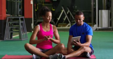 Bir tablet bilgisayar kullanarak, genç bir karışık ırk erkek kişisel eğitmen ile bir spor salonunda egzersiz genç bir karışık Yarış kadın Ön görünümü