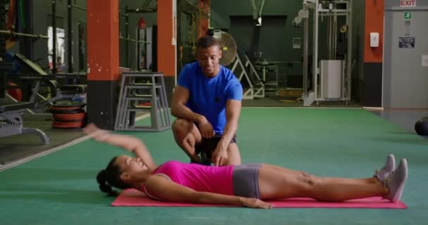 一个年轻的混合种族妇女与年轻的混合种族男性私人教练在健身房锻炼的侧视图 — 图库视频影像
