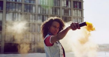 Ön görünüm yakın bir kalça genç karışık ırk kadın ayakta ve arka planda bir bina ile kentsel bir çatı üzerinde sis bombası kullanarak