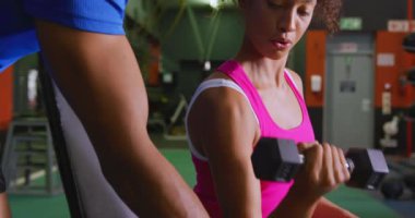 Bir dambıl kullanarak, genç bir karışık ırk erkek kişisel antrenör ile bir spor salonunda egzersiz genç bir karışık Yarış kadın yakın