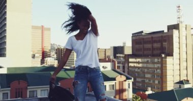 Arka planda binalar ile bir kentsel çatı üzerinde ceketini sallanan ve yuvarlak dönen bir kalça genç karışık ırk kadın Yan görünümü