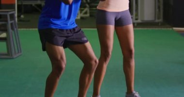 Genç bir karışık ırk erkek kişisel antrenör ile bir spor salonunda egzersiz genç bir karışık Yarış kadın Ön görünümü, birlikte dumbbells ile squats yapıyor
