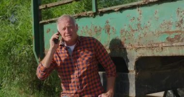Organik bir çiftlikte olgun bir Kafkas erkek çiftçinin ön görünümü, bir birleştirmek tarafından ayakta ve akıllı telefon üzerinde konuşurken