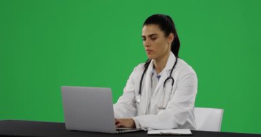 Bir dizüstü bilgisayar kullanarak ve yeşil bir arka plan üzerinde yazma genç bir Kafkas kadın doktor Ön görünümü
