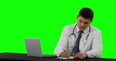 Bir dizüstü bilgisayar ve yazma kullanarak genç bir Kafkas erkek doktor Ön görünümü, yeşil ekran