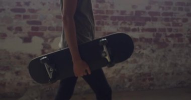 Boş bir depoda bir kalça genç karışık ırk adam Yan görünümü, bir kaykay taşıyan