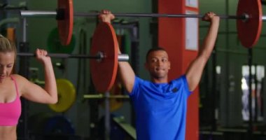 Genç bir Kafkas kadın ve genç bir karışık ırk adam bir spor salonunda egzersiz, halter kullanarak ön görünümü