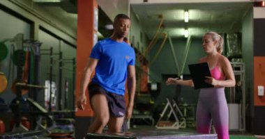 Bir pano ile genç bir Kafkas kadın kişisel antrenör ile bir spor salonunda egzersiz genç bir karışık yarış adam Yan görünümü, bir küp üzerinde atlama