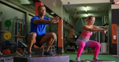 Genç bir karışık ırk adam ve genç bir Kafkas kadın bir spor salonunda egzersiz, bir küpler üzerinde atlama ön görünümü