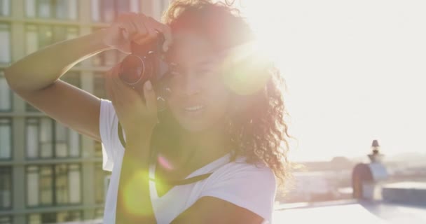 ヒップ若い混合レースの女性の正面図クローズアップは 太陽光によってバックライト付き 背景に建物と都市の屋上にカメラで写真を撮ります — ストック動画