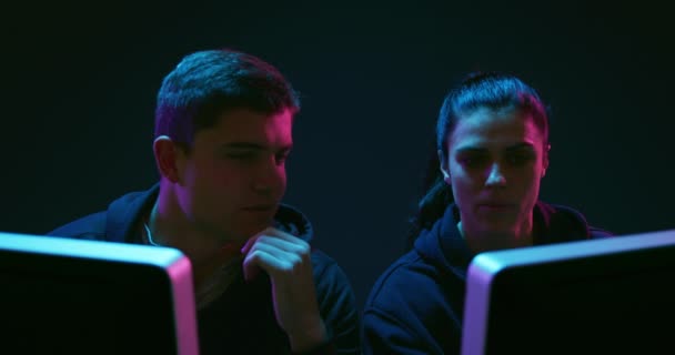 一个年轻的混血妇女和一个年轻的白人男子坐在一起 在电脑显示器前观看特写 在光线昏暗的工作区交谈 — 图库视频影像