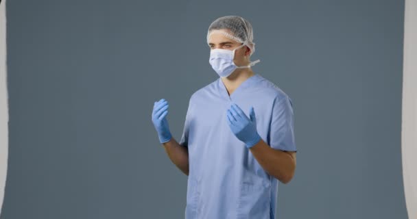 一个年轻的白种男性外科医生在灰色背景上戴着磨砂 面罩和手术手套的特写镜头 — 图库视频影像