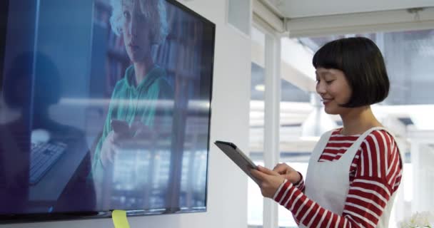 一个年轻的混血女性商业创意在现代办公室工作 使用平板电脑旁边的墙上的大显示器的侧视图 — 图库视频影像
