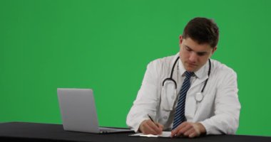 Bir dizüstü bilgisayar kullanarak ve yeşil bir arka plan üzerinde yazma genç bir Kafkas erkek doktor Ön görünümü