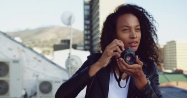Arka planda binalar ile kentsel bir çatı üzerinde bir kamera ile fotoğraf çekmek bir kalça genç karışık ırk kadın yakın
