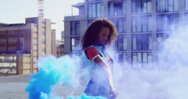 Ön görünüm yakın bir kalça genç karışık ırk kadın ayakta ve arka planda binalar ile kentsel bir çatı üzerinde sis bombası kullanarak