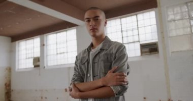 Boş bir depoda bir kalça genç karışık ırk adam Portresi, kollar kameraya bakarak geçti