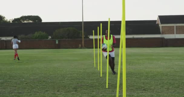 一名年轻的非洲裔美国女橄榄球手手持橄榄球球 在一个橄榄球球场的训练课上在冰道杆之间跑来跑去的镜头 — 图库视频影像