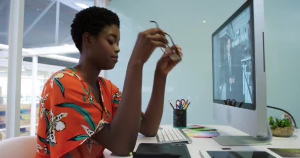 現代のオフィスで働く若いアフリカ系アメリカ人女性ビジネスクリエイティブの側面図 コンピュータを使用して 彼女の老眼鏡を取り外し 彼女の机で彼女の寺院をマッサージ — ストック動画