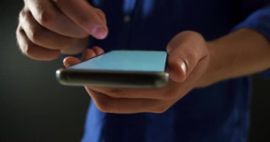 Akıllı telefon kullanarak mavi gömlek giyen, kameraya yakın tutan ve dokunmatik ekranda seçim seçen genç beyaz bir adamın ön görünümü orta bölümü