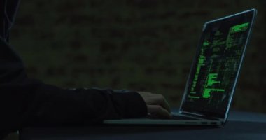 Karanlıkta bir dizüstü bilgisayarda çalışan genç beyaz bir adamın ellerinin yan görünümü, ekranda yeşil veriler görünür