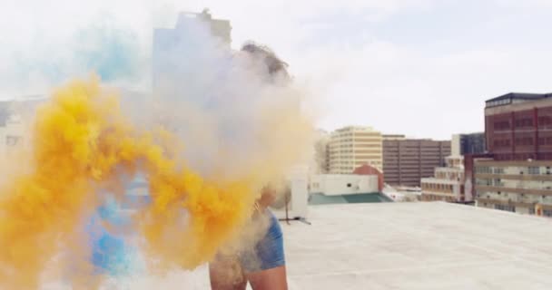 都市の屋上に2つの煙の手榴弾を立てて保持しているヒップ若い混合人種の女性の正面図 背景に建物 — ストック動画