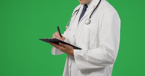 一个年轻的白种男性医生的中段的侧视图 在绿色背景上书写并拿着剪贴板 — 图库视频影像