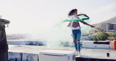 Arka planda binalar ile kentsel bir çatı üzerinde yürüyen ve sis bombası kullanan bir kalça genç karışık ırk kadın Yan görünümü