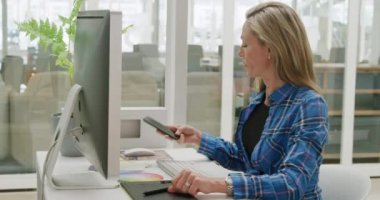 Bilgisayarı kullanan ve modern bir ofiste telefonla konuşan beyaz bir kadın iş dünyasının yan görüntüsü.