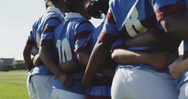 Rugby sahasında kolları bağlı duran, rugby maçına hazırlanan genç, yetişkin, çok ırklı bayan rugby oyuncularından oluşan bir takımın orta kısmı.