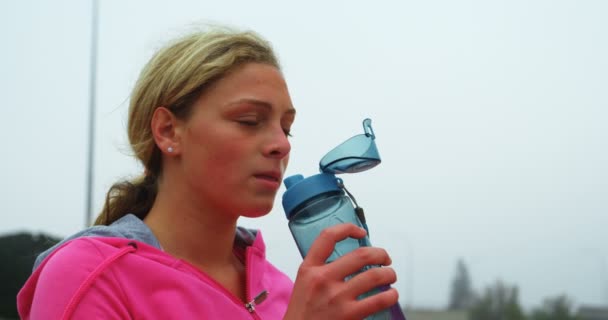 スポーツ会場で水を飲む若い白人女性アスリートの正面図 彼女はスポーツ会場4Kに立っています — ストック動画