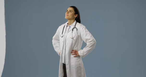 一个年轻的白种女医生微笑 在灰色背景上用双手仰望臀部的正面视图 — 图库视频影像