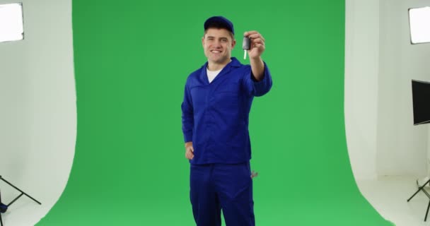 一个年轻的白种人杂工穿着蓝色工作服和帽子拿着钥匙 在绿色背景上微笑的正面视图 — 图库视频影像
